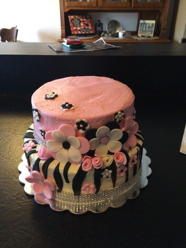 A pink and black cake decorated with flowers and zebra stripes.