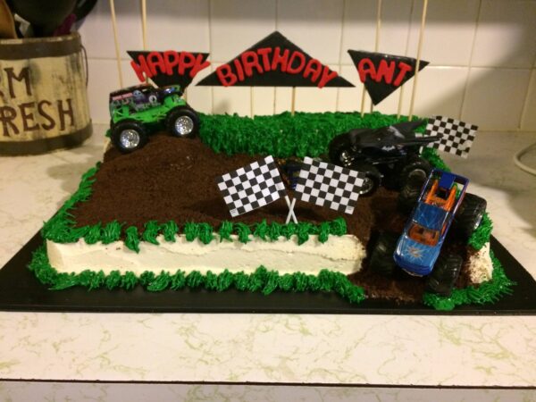 A birthday cake with monster trucks and a checkered flag.