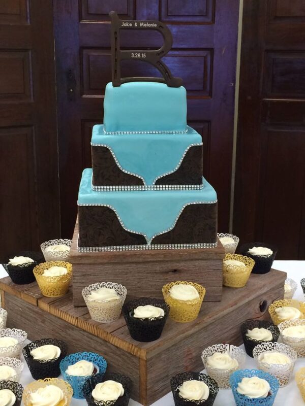 A wedding cake with cupcakes on a wooden stand.