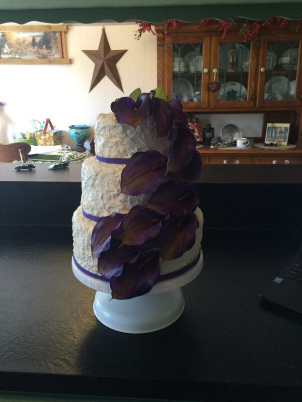 A three tier cake with purple flowers on top.