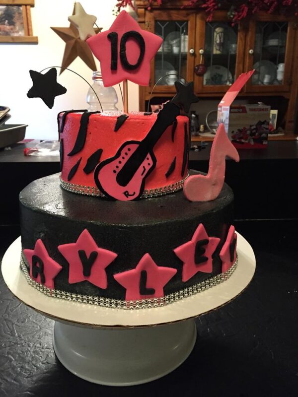 A pink and black cake decorated with stars and a guitar.