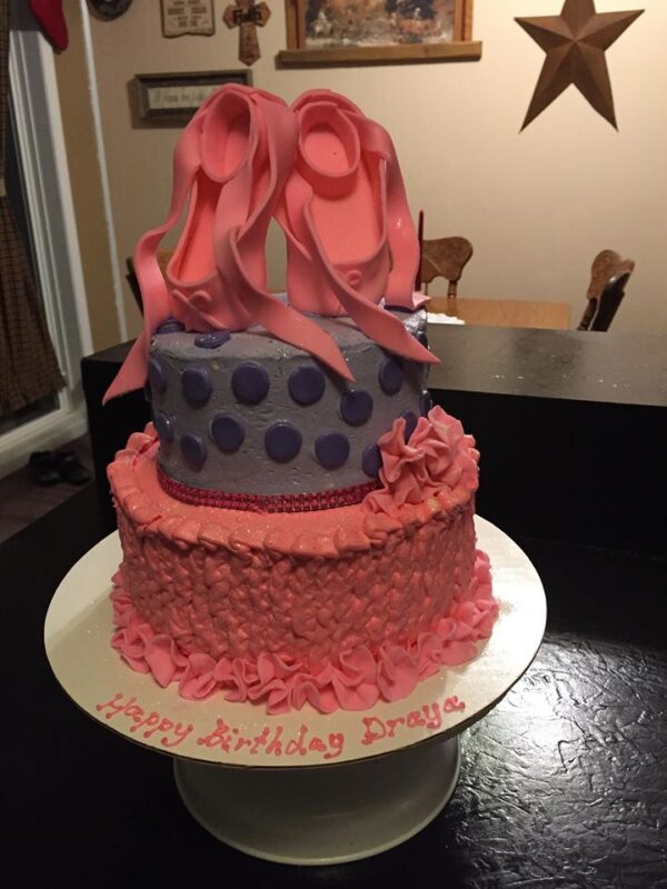 A pink and purple cake with a pair of shoes on top.