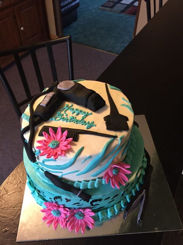 A birthday cake decorated with a hair dryer and flowers.