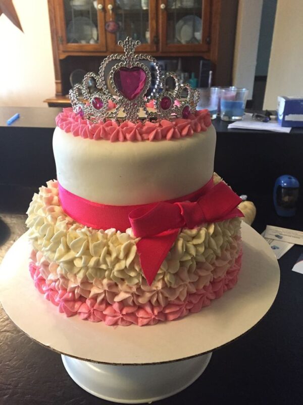 A pink and white cake with a tiara on top.