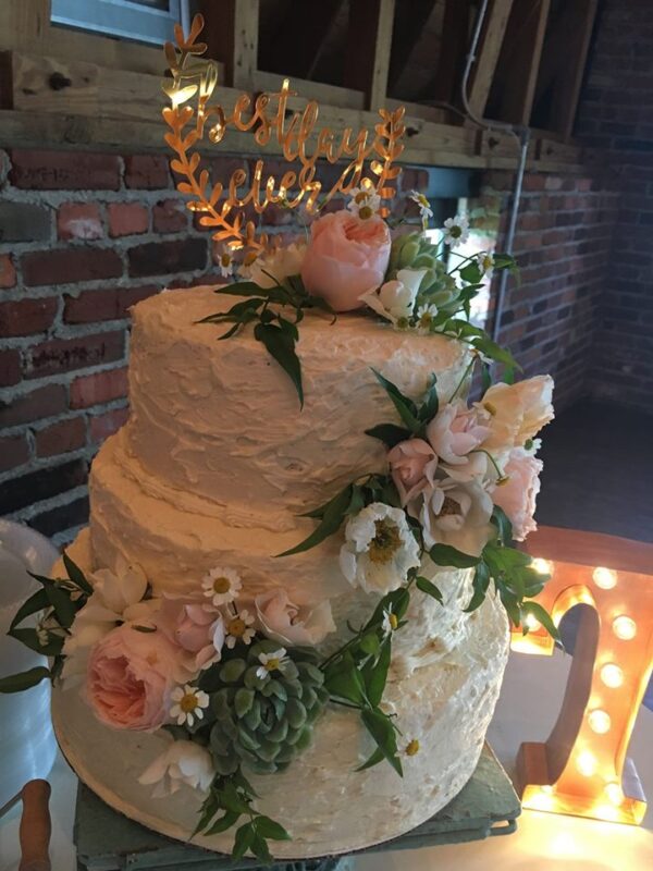 A three tier wedding cake with flowers on top.