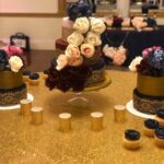 A wedding cake with flowers and cupcakes on a table.