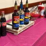 A table full of coca cola bottles on a pink tablecloth.