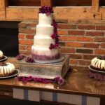 A three tiered wedding cake with purple flowers on top.