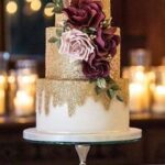 A gold and burgundy Tiered Cake on a stand.