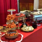 A table full of food and desserts on a red tablecloth.