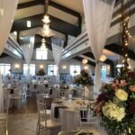 A wedding reception in a large room with white tablecloths and chandeliers.