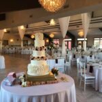 A wedding cake sits on a table in a large room.