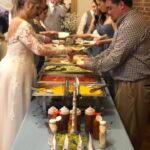 A bride and groom serving food from a buffet table.