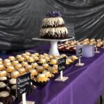 A table full of cupcakes on a purple tablecloth.