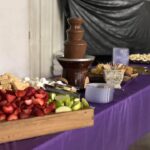 A purple table with a chocolate fountain and fruit on it.