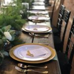 A long table set with gold plates and greenery.