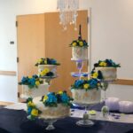 A wedding cake with blue and yellow flowers on top.