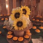 A cake with sunflowers and cupcakes on a wooden table.