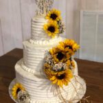 A white wedding cake with sunflowers on top.