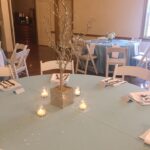 A blue table setting with candles and white tablecloths.