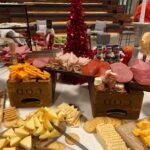 A table full of cheese and crackers with a christmas tree in the background.