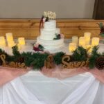 A wedding cake on a table with candles and pine cones.