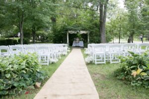 An outdoor wedding ceremony set up with white chairs and a tarp.