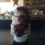 A three tier cake with purple flowers on top.