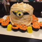 A cake decorated like a minion with pumpkins and cupcakes.