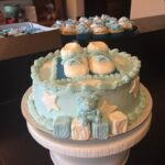 A blue baby shower cake with cupcakes on top.