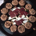 A black plate with cupcakes and roses on it.