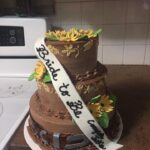 A three tier cake decorated with sunflowers and a sash.