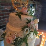 A three tier wedding cake with flowers on top.