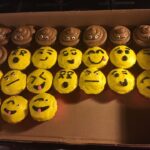 A box of cupcakes decorated with emoji faces.