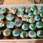 A box of cupcakes decorated with cows and cactus.