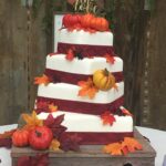 A wedding cake decorated with fall leaves and pumpkins.