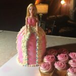 A barbie cake with cupcakes next to it.