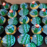 A box of cupcakes decorated with fish and other decorations.