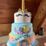 A unicorn birthday cake with a mustache and rainbows.