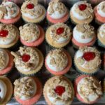 A tray of cupcakes with icing and a cherry on top.