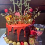 A birthday cake with a bottle of bourbon on top.