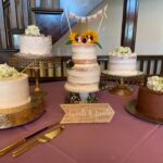 Four wedding cakes on a table in front of a purple tablecloth.