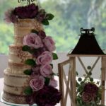 A wedding cake with purple flowers and a lantern on top.