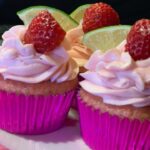 Three pink cupcakes with strawberries and limes on a plate.