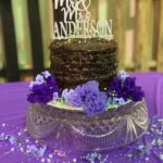 A cake decorated with purple flowers and a mr and mrs cake topper.