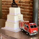 A wedding cake with a toy fire truck on it.