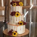 A wedding cake with sunflowers and a monogram on top.