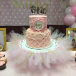 A cake with pink tulle and cupcakes on a table.