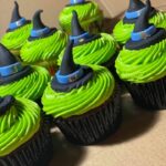 A box of green cupcakes with witch hats on them.