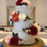 A three tier wedding cake with red and white flowers.